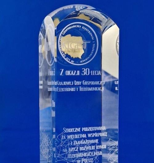 złota statuetka szklany obelisk. Szklana statuetka z okazji jubileuszu 30-lecia Krajowej Izby Gospodarczej Elektroniki i Telekomunikacji. Życzenia oraz grafika związana z telekomunikacją grawerowane 3D wewnątrz szkła, do wykonania logo wykorzystaliśmy 3 techniki zdobienia grawerowanie 3D, piaskowanie oraz malowanie natryskowe na złoty kolor Poszczególne elementy grafiki są wygrawerowane na różnych głębokościach