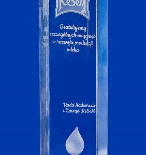 szklana statuetka z kroplą w 3D dla branży mleczarskiej, kryształowa statuetka z gratulacjami grawerowanymi laserem wewnątrz szkła Szklana statuetka na niebieskiej podstawce z imiennymi gratulacjami od Kesem Statuetka z grawerem 3D na podstawce z pięknego niebieskiego kryształu