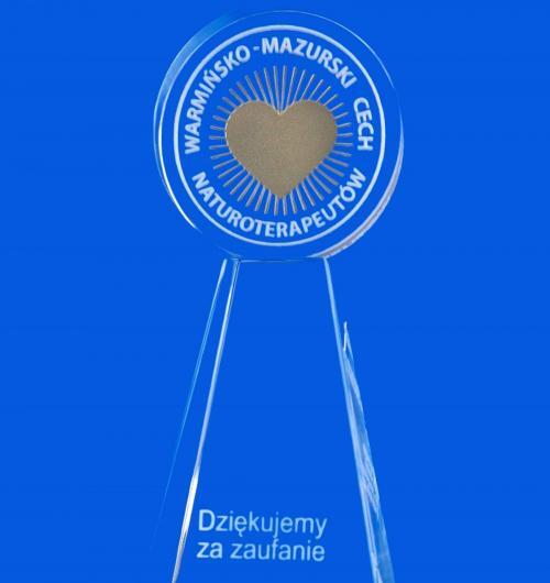 szklana statuetka z okazji jubileuszu założenia Cechu. Kryształowa statuetka z medalem, na którym jest złote logo. Złote serce z logo jest na medalu a podziękowanie za zaufanie grawerowane w cokole statuetki. Kryształowa statuetka z okazji jubileuszu Warmińsko-Mazurskiego Cechu Naturoterapeutów