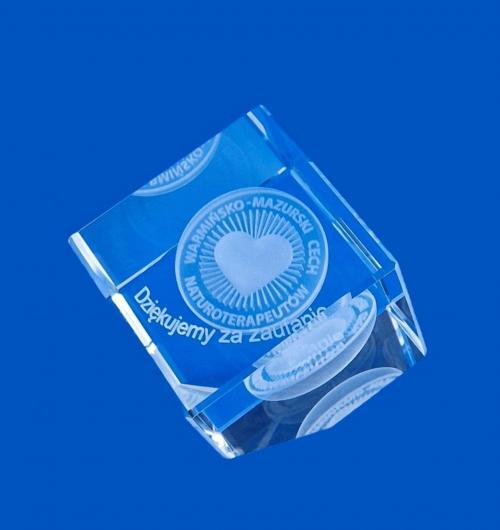 szklany upominek biznesowy z okazji jubileuszu Warmińsko-Mazurskiego Cechu Naturoterapeutów Kryształowy sześcian ze ściętym narożnikiem z wygrawerowanym sercem w 3D i logo Cechu Szklana kostka z grawerem 3D logo jako drobny firmowy upominek