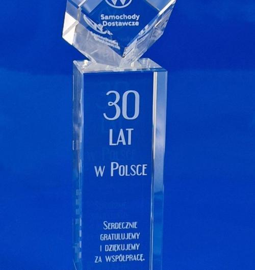 szklana statuetka z okazji 30-lecia Volkswagen Polska od AHK, kryształowa statuetka z gratulacjami z okazji 30-lecia istnienia w Polsce. Kryształowa bryła z sześcianem na górze, w którym jest wygrawerowane laserem logo