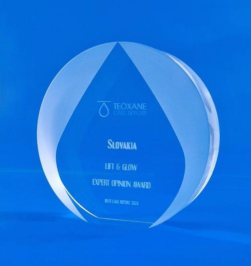 Okrągła statuetka ze szkła kryształowego z delikatnym ścięciem na dole. Na statuetce bardzo efektownie wypiaskowana kropla nawiązująca do logo firmy. Szklana nagroda dla ekspertów firmy Teoxane. Personalizowane szklane statuetki w kształcie koła z piaskowaną kroplą