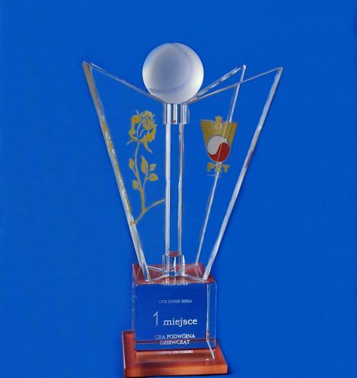 szklana statuetka na turniej tenisa - Polski Związek Tenisowy Szklana statuetka na zamówienie na zawody OTK Super Seria Szklana statuetka składa się z wyciętych szklanych skrzydeł, na których jest logo i róża (symbol turnieju) podstawka to kryształowy sześcian, wewnątrz którego jest wygrawerowana laserem 3D nazwa i kategoria turnieju Podstawka jest z czerwonego szkła nawiązującego do koloru w logo PZT Oryginalna szklana statuetka zaprojektowana przez naszych doświadczonych grafików Jesteśmy polskim producentem statuetek od 2000 roku