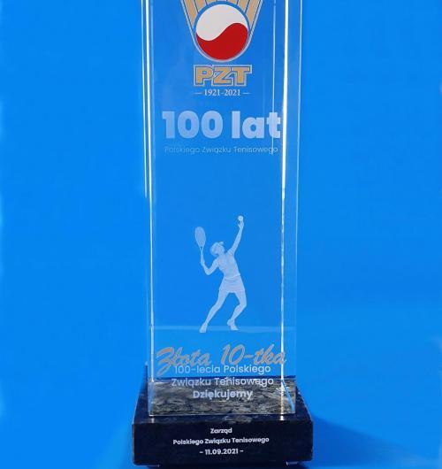 szklana statuetka trofeum sportowe Złota Dziesiątka polskiego tenisa Szklana statuetka 3D z wygrawerowaną tenisistką jako podziękowanie dla najlepszych zawodników z okazji 100-lecia PZT Kryształowa statuetka na kamiennej podstawie z jubileuszowym logo w kolorze Na podstawie z czarnego kamienia wypiaskowany i malowany na biało napis