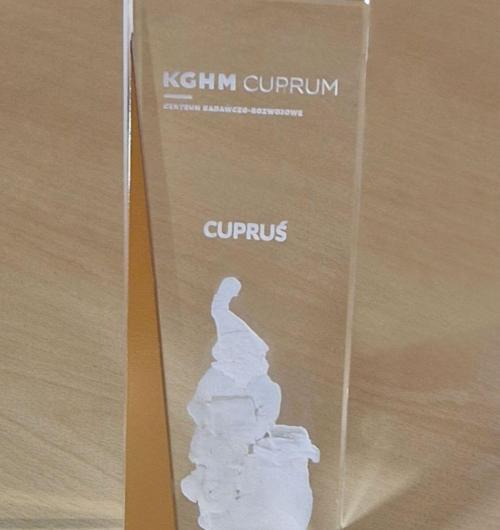 szklana statuetka z metalem z krasnalem Cuprusiem wykonana na zamówienie KGHM CUPRUM Centrum Badawczo-Rozwojowe Statuetka ze szkła kryształowego delikatnie zwęża się ku górze, z boku ozdobny element ze stali nierdzewnej pomalowany na kolor miedziany Krasnal Cupruś grawerowany wewnątrz szkła, całość tworzy bardzo ekskluzywny upominek firmowy Laser 3D producent statuetek na zamówienie od 2000 roku, Zielona Góra