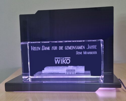 Glass award with a 3D company building placed on an elegant black, LED-illuminated base The building is engraved in a crystal glass block as a three-dimensional object The glass statuette with a 3D building is a retirement gift for a company owner. This exclusive glass gift comes with an illuminated base with a remote control, allowing you to freely change the backlight colors. If you are looking for an elegant and modern, personalized corporate gift, ask us; we have been providing 3D engraving for 25 years. Lase 3D glass award manufacturer from Zielona Gora in Poland