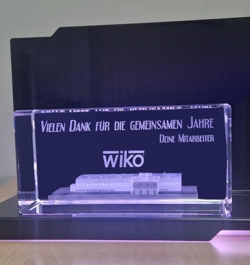 szklana statuetka z budynkiem firmy w 3D umieszczona na eleganckiej czarnej, podświetlanej podstawce z diodami LED Budynek wygrawerowany w kryształowej bryle szkła jako obiekt trójwymiarowy Szklana statuetka z budynkiem 3D to prezent dla właściciela firmy z okazji przejścia na emeryturę Ekskluzywny szklany prezent jest w zestawie z podświetlaną podstawką na pilota, dzięki któremu można dowolnie zmieniać kolory podświetlenia Jeżeli szukasz eleganckiego i nowoczesnego, personalizowanego prezentu firmowego zapytaj u nas, już od 25 lat zajmujemy się grawerowaniem 3D Laser 3D producent szklanych statuetek z Zielonej Góry